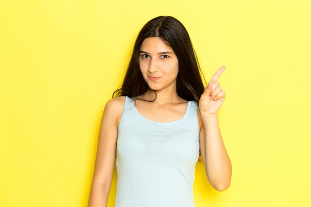 Una mujer joven de vista frontal en camisa azul posando y sonriendo sobre el fondo amarillo pose de niña modelo belleza joven