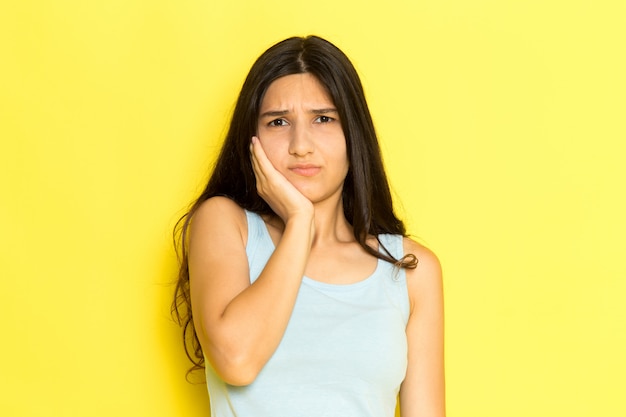 Una mujer joven de vista frontal en camisa azul que tiene un dolor de muelas en el fondo amarillo pose de niña modelo belleza joven