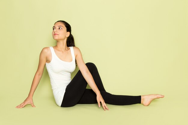 Una mujer joven de vista frontal con camisa blanca y pantalón negro posando sentada en pose de yoga meditando