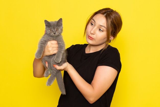 Una mujer joven de vista frontal en vestido negro con lindo gatito en amarillo