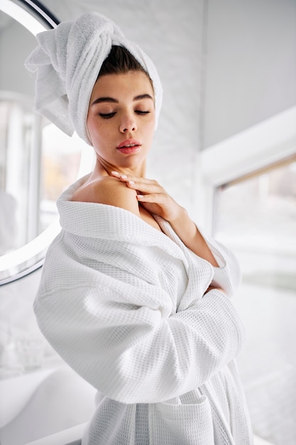 Foto gratuita mujer joven vistiendo una bata de baño y una toalla en el pelo