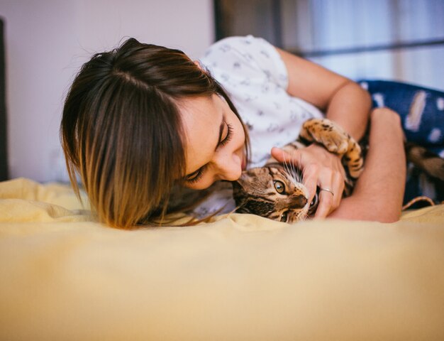La mujer juega con el gato de Bengala en la cama