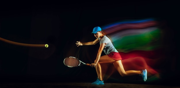Una mujer jugando al tenis aislado en la pared negra en luz mixta y stobe