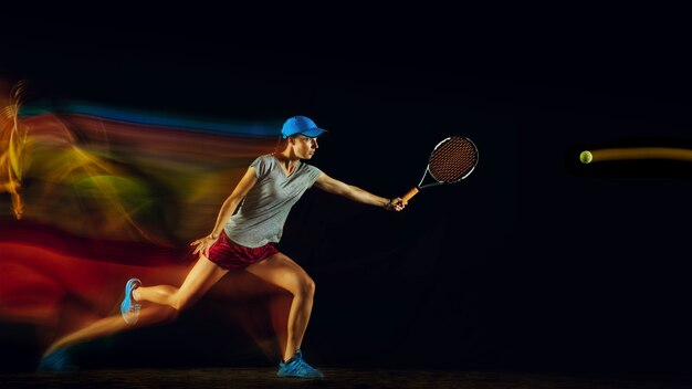 Una mujer jugando al tenis aislado en la pared negra en luz mixta y stobe