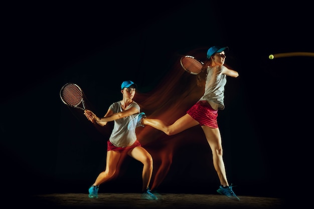 Una mujer jugando al tenis en diferentes posiciones aislado en la pared negra en luz mixta y stobe