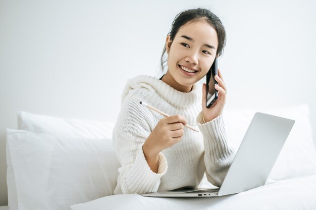 Mujer jugando portátil y hablando por teléfono.