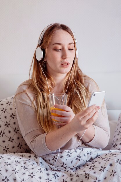 Mujer con jugo de navegación smartphone en la cama