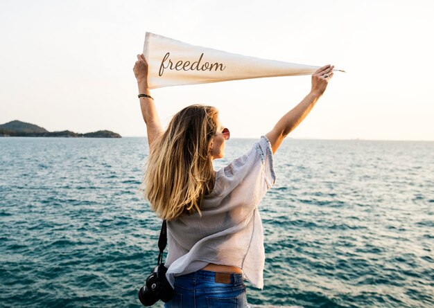 Mujer junto al mar sosteniendo la bandera con la inscripción de la libertad
