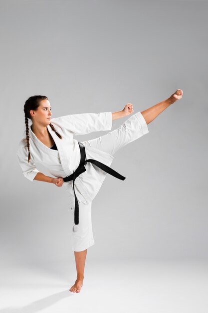 Mujer de karate de lado en kimono blanco tradicional sobre fondo blanco.
