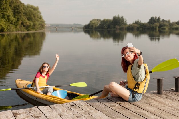 Mujer en kayak con amigo tomando selfie en muelle