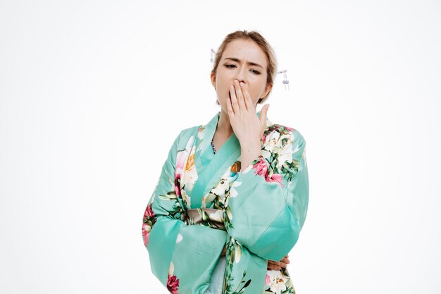 Mujer en kimono japonés tradicional con aspecto cansado y aburrido bostezo sosteniendo la mano en la boca en blanco