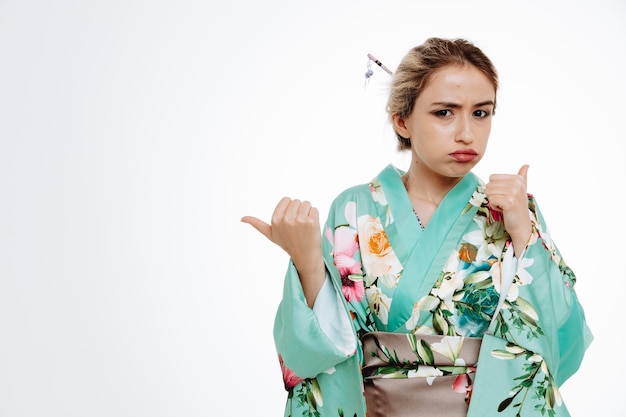 Mujer en kimono japonés tradicional disgustado soplando mejillas apuntando con los pulgares a los lados en blanco