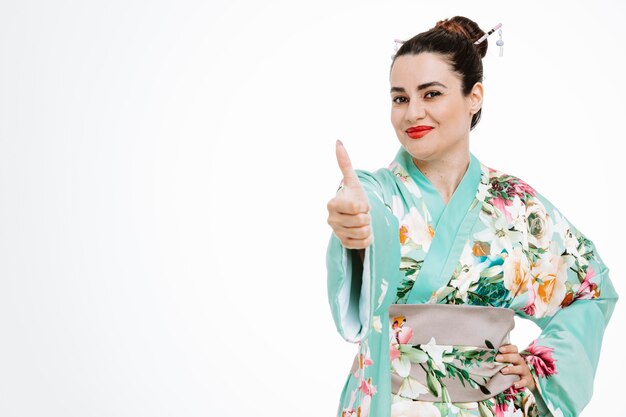 Mujer en kimono japonés tradicional feliz y complacido mostrando el pulgar hacia arriba en blanco