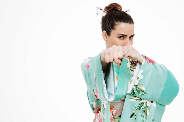 Mujer en kimono japonés tradicional con rostro serio mostrando puños posando como un luchador en blanco