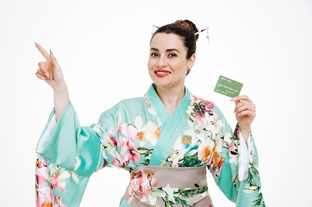 Mujer en kimono japonés tradicional con tarjeta de crédito apuntando con el dedo índice hacia el lado en blanco