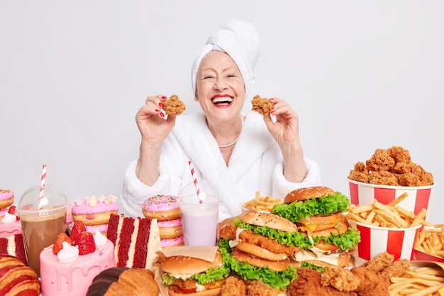 Mujer con labios rojos sostiene dos pepitas come comida trampa vestida con albornoz rodeado de alimentos poco saludables en blanco