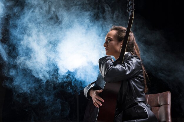 Mujer de lado abrazando la guitarra y el humo del escenario