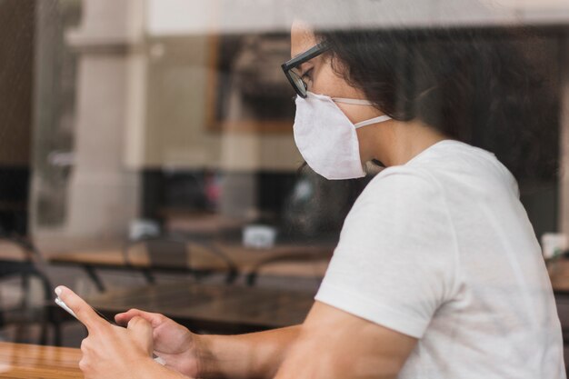 Mujer de lado con máscara médica revisando su teléfono