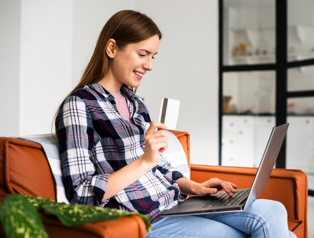 Mujer de lado mirando su laptop y sosteniendo una tarjeta de crédito