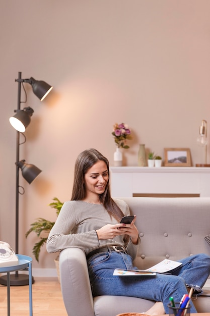 Foto gratuita mujer de lado sentada en el sofá y trabaja en su teléfono