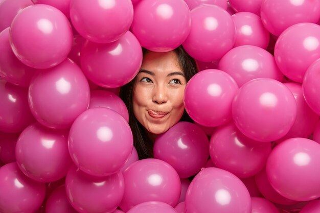 Mujer lame los labios con la lengua concentrada arriba cuidadosamente rodeada de globos rosados inflados