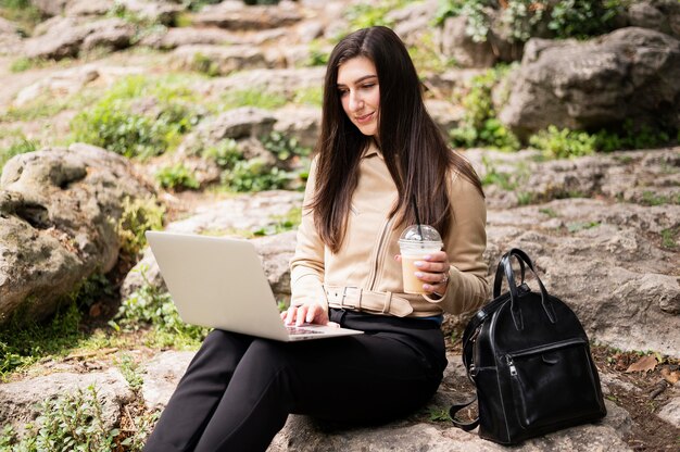 Mujer con laptop y bebida trabajando al aire libre