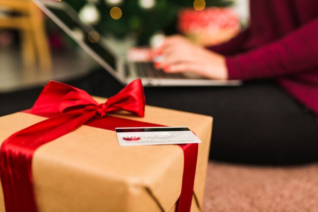 Mujer con laptop cerca de tarjeta de crédito y caja de regalo