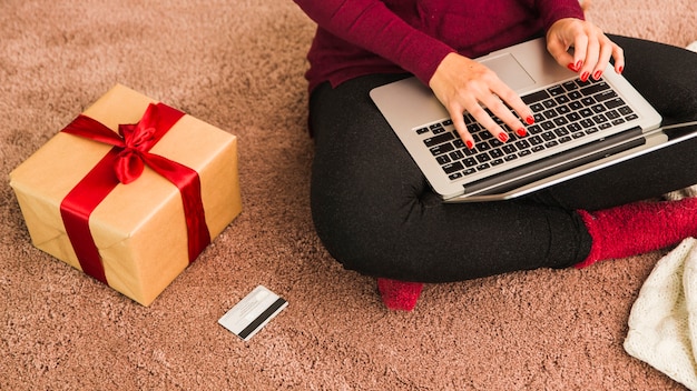 Mujer con laptop cerca de tarjeta plástica y caja de regalo