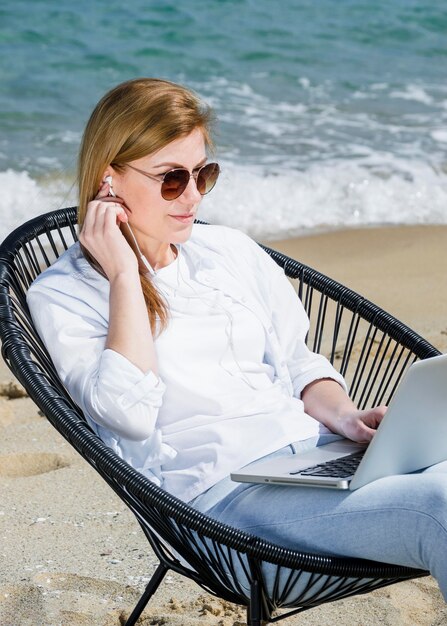 Mujer con laptop y gafas de sol trabajando en la playa