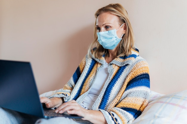 Mujer con laptop y mascarilla médica en cuarentena