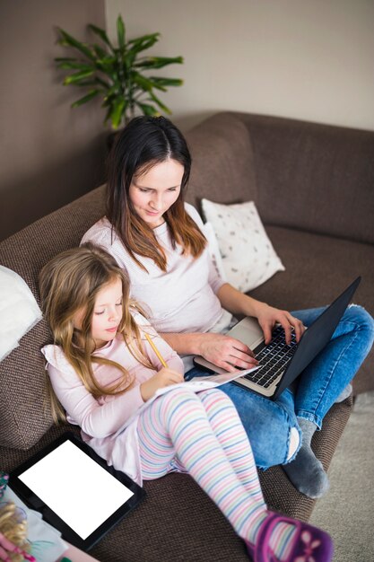 Mujer con laptop mirando a su hija estudiando