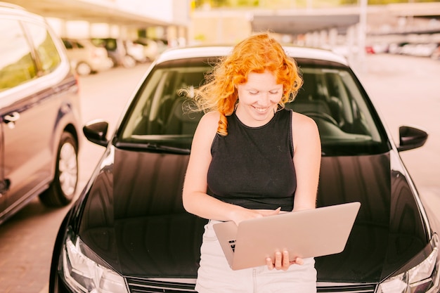 Foto gratuita mujer con laptop sentada en el capó del auto