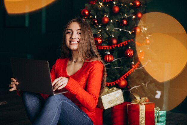 Mujer con laptop sentada junto a árbol de navidad