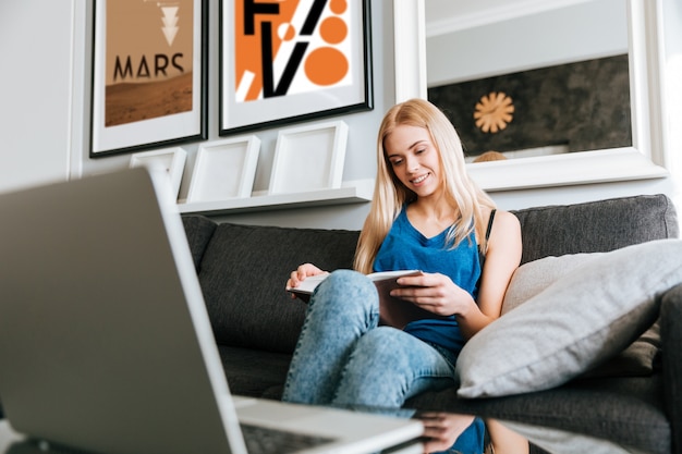 Foto gratuita mujer con laptop en su mesa leyendo un libro en casa