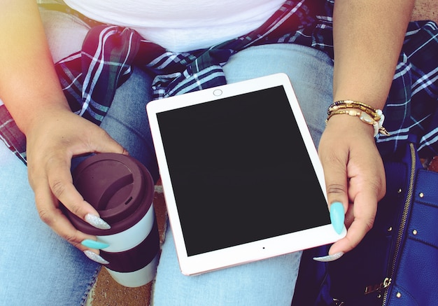 Mujer con largas uñas coloridas sosteniendo una taza de café y una tableta