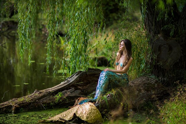 mujer con largo cabello castaño y vestida como una sirena se sienta en la piedra sobre el agua