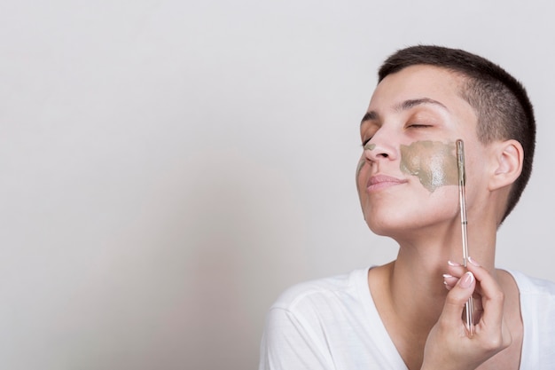 Foto gratuita mujer lateral aplicando en el tratamiento de lodo de mejilla