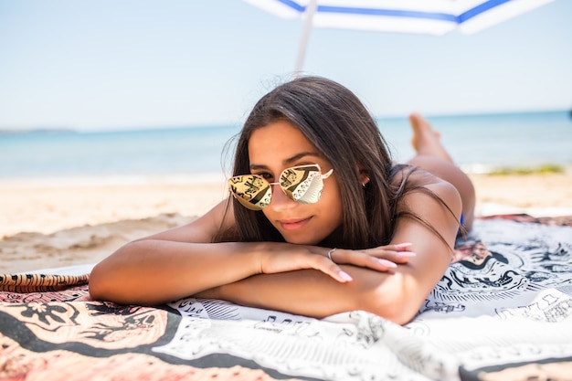 Mujer latina joven tumbado en la arena bajo la sombrilla en la playa del mar. vocación de verano