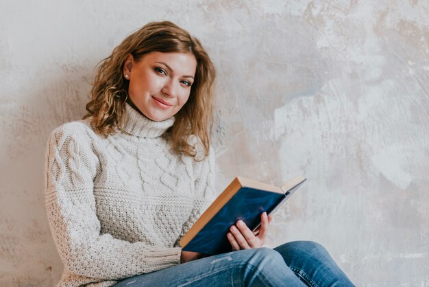 Mujer de lectura junto a la pared mirando a la cámara