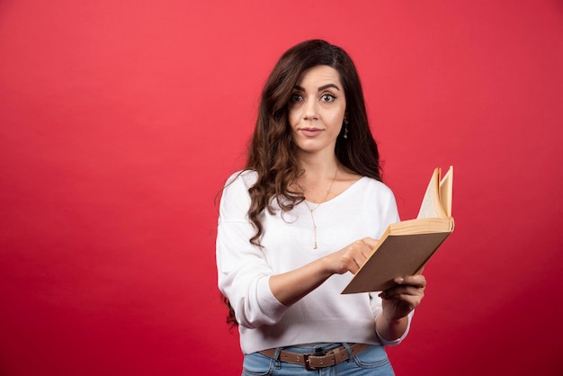 Mujer de lectura de libros de pie sobre un fondo rojo. Foto de alta calidad