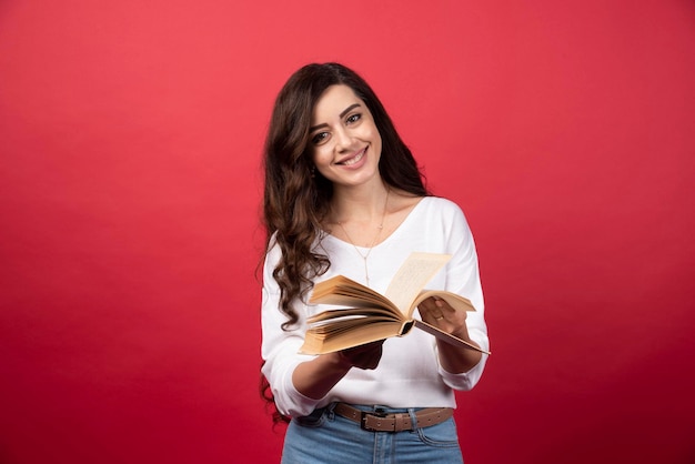 Mujer de lectura de libros de pie sobre un fondo rojo. Foto de alta calidad