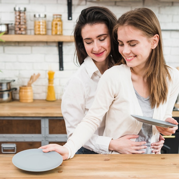 Mujer lesbiana sonriente que sirve platos en la mesa de madera en la cocina