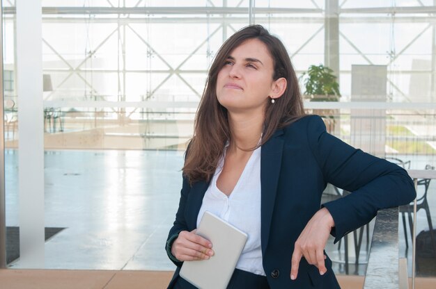 Mujer levantando la cabeza, pensando, sosteniendo la tableta en la mano