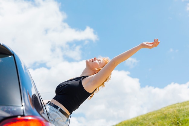 Mujer levantando la mano al cielo por la ventana del coche en un día soleado