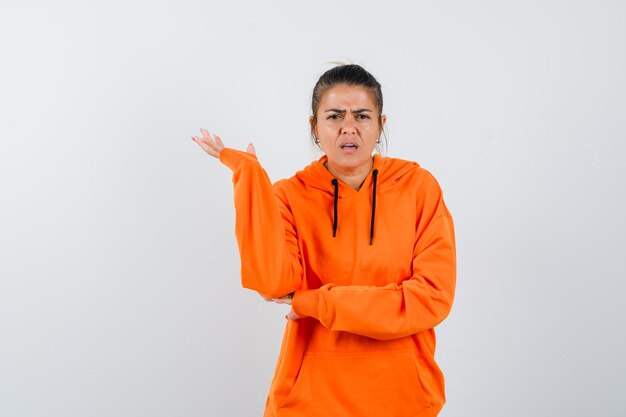 Mujer levantando la mano en gesto de desconcierto en sudadera con capucha naranja
