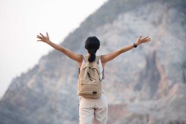 Foto gratuita mujer levantando las manos en la cima de una montaña mientras camina y postes de pie sobre una cresta de montaña rocosa mirando valles y picos.