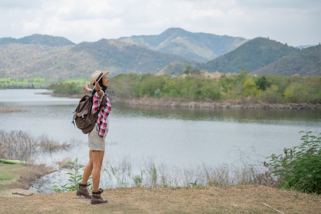 mujer levantando las manos a orillas del lago / excursionista de mujer asiática en el frente sonriendo feliz, mujer de senderismo en el bosque, cálido día de verano.