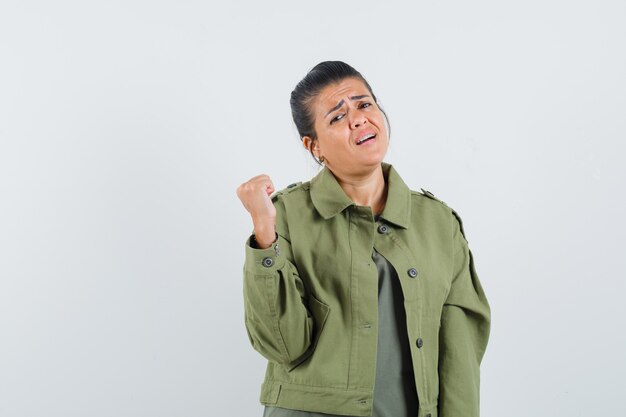 Mujer levantando el puño cerrado en chaqueta, camiseta y mirando triste