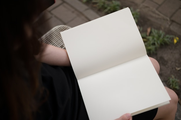 Mujer leyendo el libro en blanco en el jardín