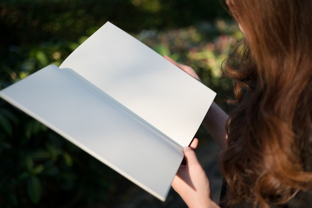 Mujer leyendo el libro en blanco en el jardín